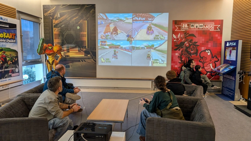 Plusieurs personnes jouent à Mario Kart, assises sur des canapés.