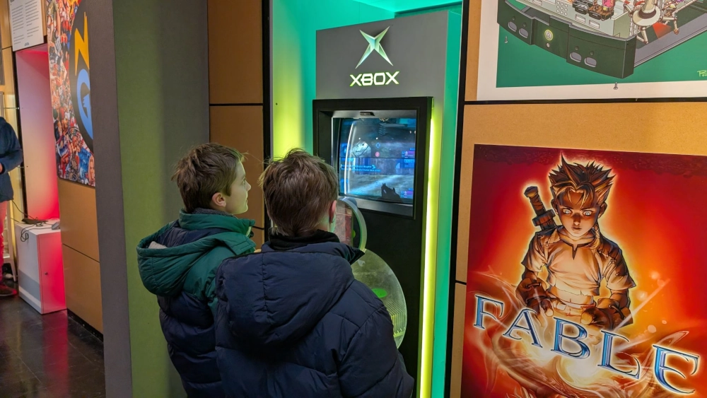 Deux garçons jouent à la première console Xbox sur un kiosque dédié.